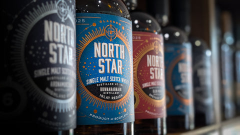 A selection of North Star Independent bottles on a shelf focusing on a bunnahabhain bottling. The label is a vibrant blue with North Stars iconic compass style logo. 