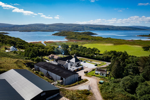 A shot of the ardnamurchan taken from a drone at distance. The whole distillery can be seen with the coast line in the background on a bright sunny day.