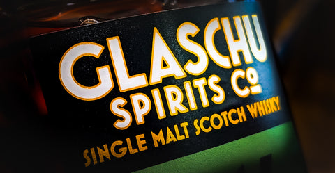 A close up shot of Glaschu independent bottlers single malt. Glaschu Spirits Co written in white with a yellow outline and single malt scotch whisky in gold smaller writing below. 