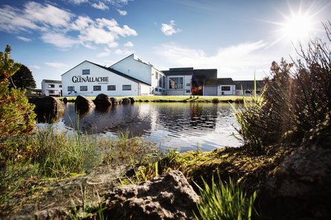 the glenallachie distillery seen from the other side of a loch with the glenallachie sign on the side of the white building on a bright sunny day 